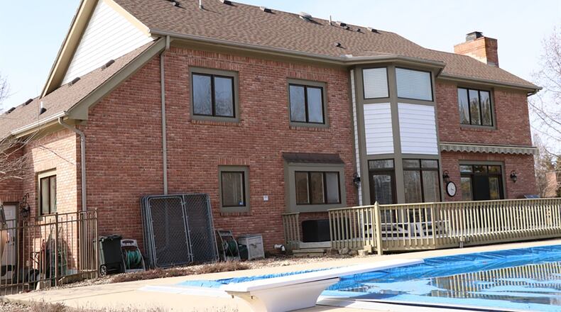 The great room’s wall of windows with transoms above looks out over the backyard pool deck. A wrought-iron fence surrounds an in-ground swimming pool and composite deck.