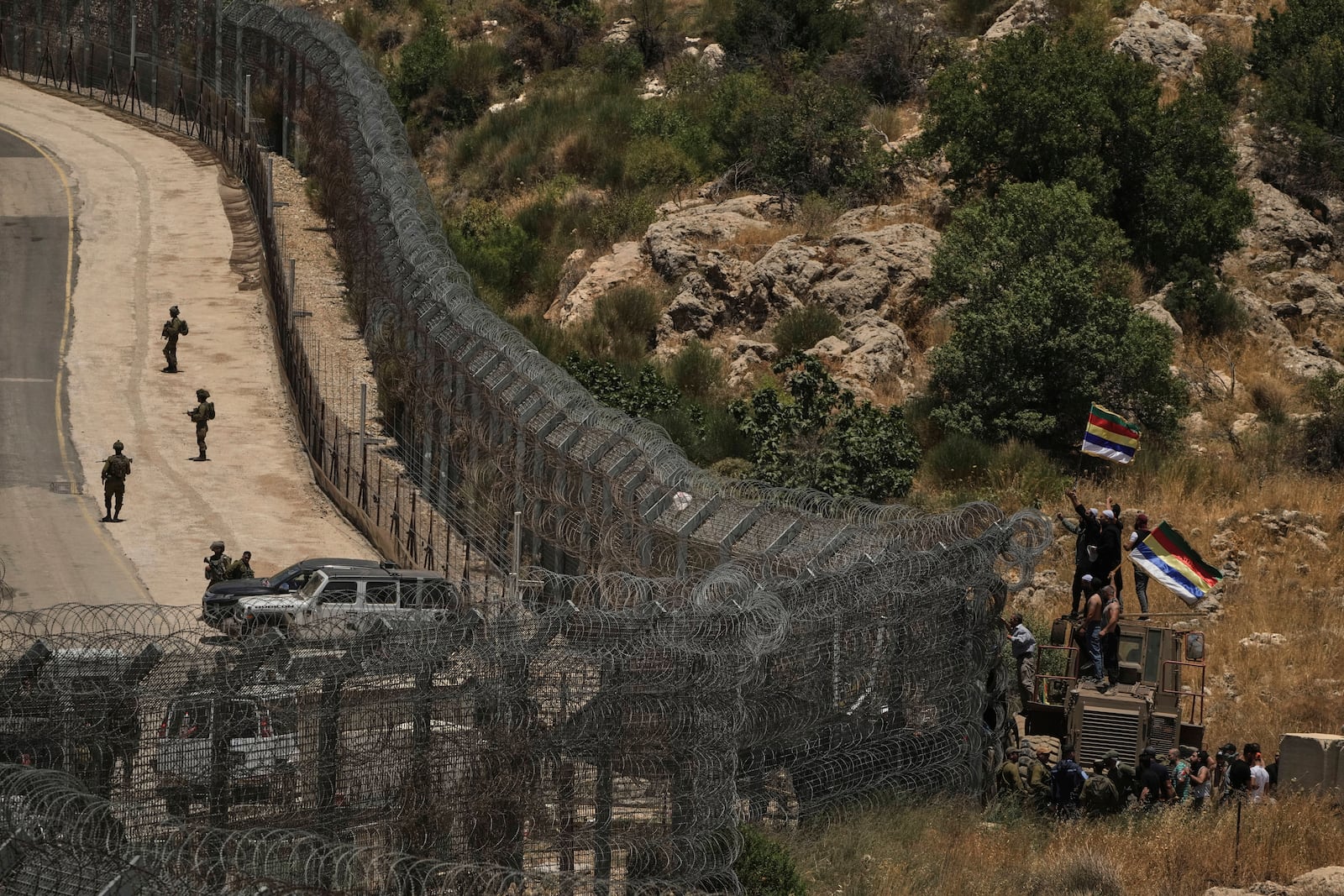 Israeli soldiers stand guard as Syrian Druze protest near the Israeli-Syrian border, as seen from the town of Majdal Shams in the Israeli-controlled Golan Heights, Wednesday, July 16, 2025, amid ongoing clashes between Syrian government forces and Druze armed groups in the southern Syrian city of Sweida. (AP Photo/Leo Correa)