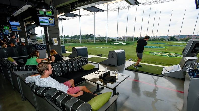 Jay Takach, left, watches Trey Greene hit a golf ball during a preview day at Topgolf in July 20023 at the West Chester Township location. The three-level, 64,232-square-foot facility in the Streets of West Chester features 102 climate-controlled hitting bays that are able to host up to six players at one time. NICK GRAHAM/STAFF