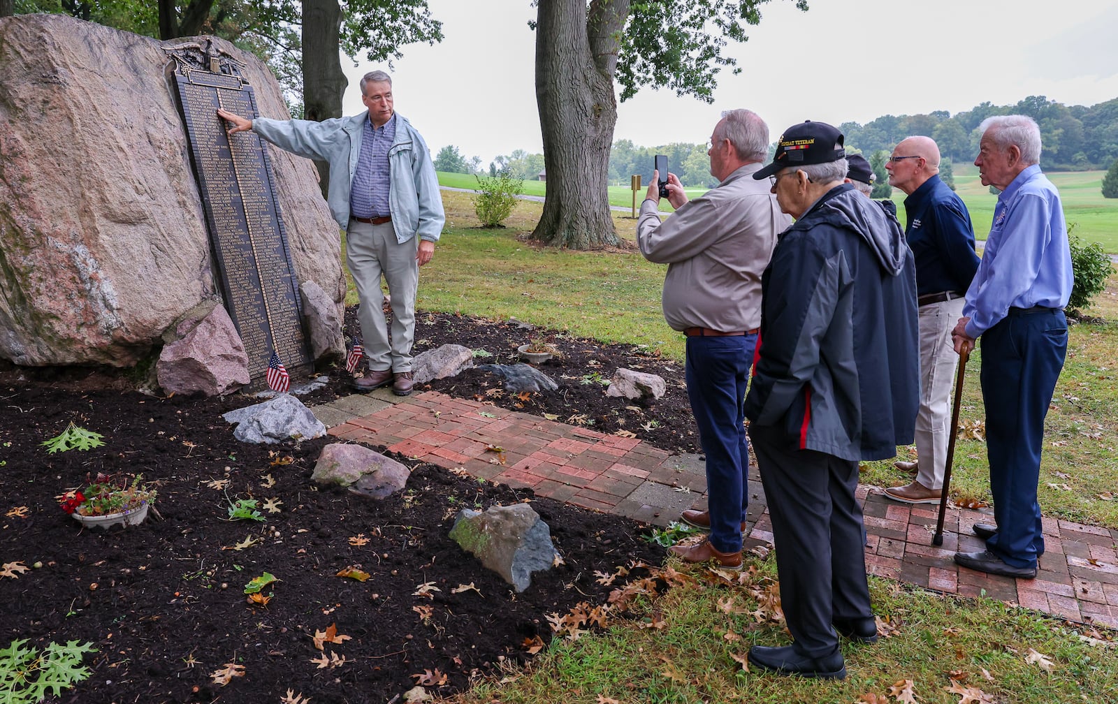 Jim Cunningham (left), an adult leader and former scoutmaster of Scouting America Troop 193, talks about Victory Oak Knoll Memorial as members of the Montgomery County Veterans Services Commission listen on Wednesday, Sept. 24, 2025, in Kettering. Cunningham helped oversee repairs to the memorial, which was damaged in a windstorm last fall. The veterans commission provided funds for repairs. BRYANT BILLING / STAFF