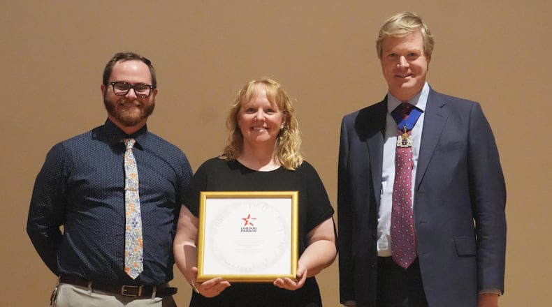 Troy High School Associate Band Director Casey Layer (left) and THS Director of Bands Molly Venneman (center) accept an invitation from parade representative Duncan Sandys to perform in the 2027 London Parade on Jan. 1, 2027. The Troy High School marching band has been every four years since first performing in 2002. CONTRIBUTED