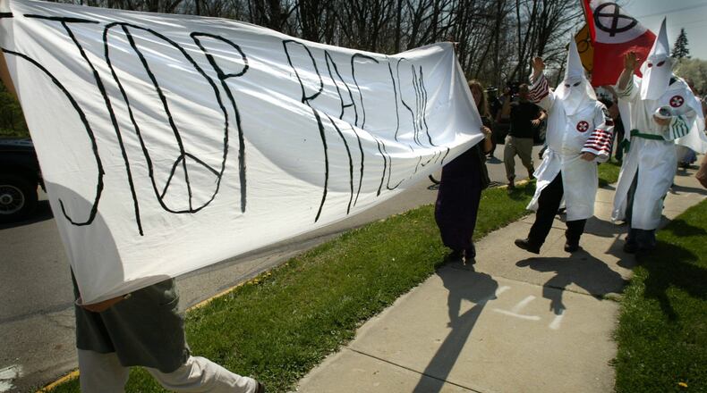 As hooded and robed members of the Ku Klux Klan walk down a sidewalk in Yellow Springs to protest racial discrimination against whites, protesters to their appearance carry a “stop racism” sign. Hundreds of protesters gathered to show their disapproval to the KKK’s protest, and the event was without arrests. JIM WITMER / STAFF
