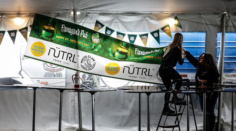 From left, Holly Pierce and Stephanie Markham hang banners in a large tent at Flanagan's Pub Thursday, March 16, 2023, in preparation of St. Patrick's Day. JIM NOELKER/STAFF