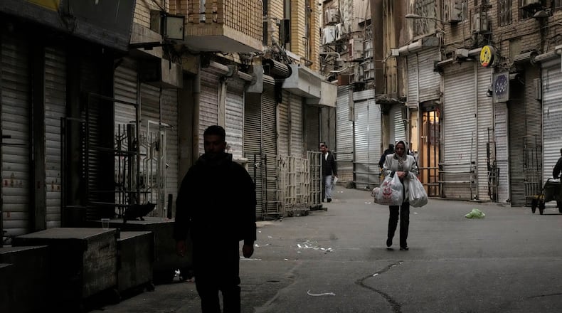 A woman carries her groceries as people walk along the mostly empty Tehran traditional main bazaar, where most shops are closed, in Tehran, Iran, Tuesday, March 10, 2026. (AP Photo/Vahid Salemi)