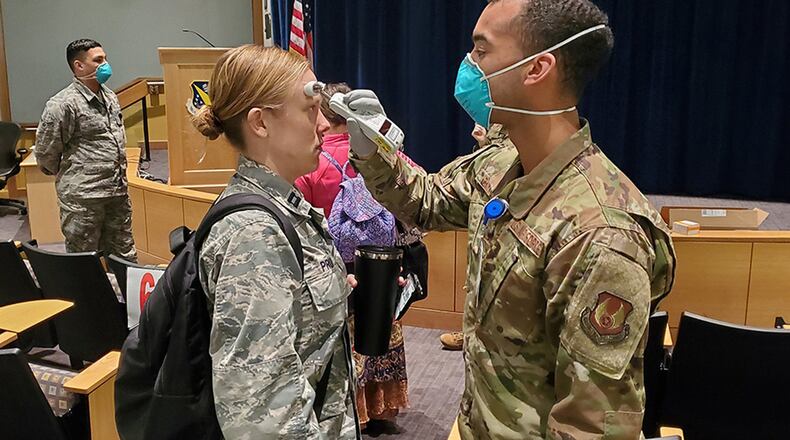 Airman 1st Class Luis Cintron, a dental technician at the Wright-Patterson Medical Center, takes a temperature reading from Capt. Kelsey Pruitt, a nurse practitioner with the Women’s Health Center as she arrives for duty March 25. All medical center staff members are now having their temperatures checked upon arriving at the facility for duty at one specified location. (U.S. Air Force photo/Bryan Ripple)