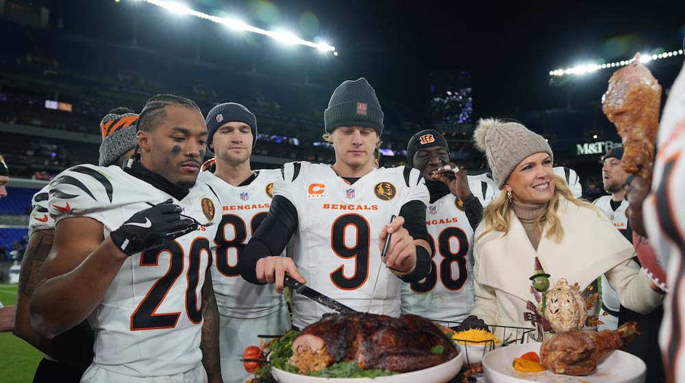Cincinnati Bengals quarterback Joe Burrow (9) joined by NBC Sports sideline reporter Melissa Stark, right, teammates DJ Turner II (20), Mike Gesicki (88), and DJ Ivey (38) carves a turkey after NFL football game against the Baltimore Ravens, Thursday, Nov. 27, 2025, in Baltimore. (AP Photo/Stephanie Scarbrough)