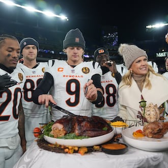 Cincinnati Bengals quarterback Joe Burrow (9) joined by NBC Sports sideline reporter Melissa Stark, right, teammates DJ Turner II (20), Mike Gesicki (88), and DJ Ivey (38) carves a turkey after NFL football game against the Baltimore Ravens, Thursday, Nov. 27, 2025, in Baltimore. (AP Photo/Stephanie Scarbrough)
