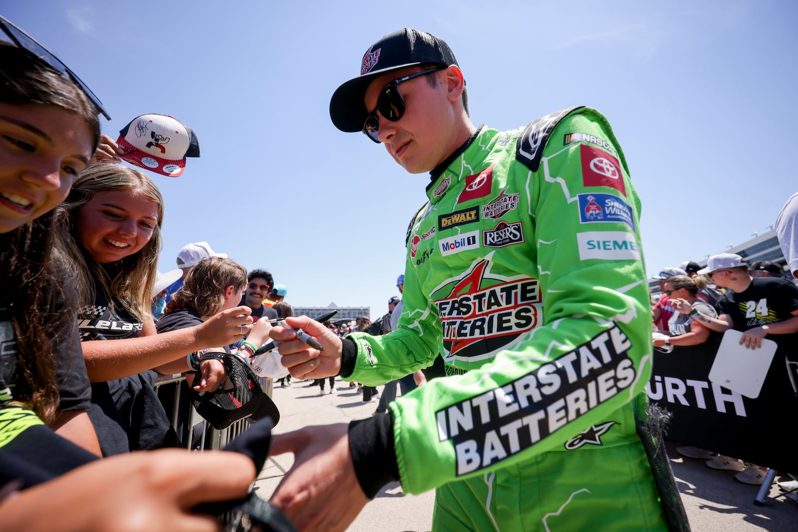 Christopher Bell, right, autographs a fan's shirt before a NASCAR Cup Series auto race at Texas Motor Speedway in Fort Worth, Texas, Sunday, May 4, 2025. (AP Photo/Gareth Patterson)