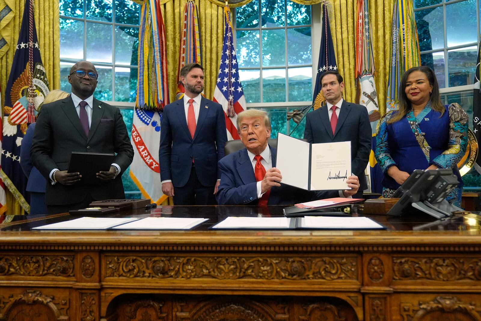 President Donald Trump holds up a signed document to present to Congo's Foreign Minister Therese Kayikwamba Wagner, right, as Rwanda's Foreign Minister Olivier Nduhungirehe, from left, Vice President JD Vance and Secretary of State Marco Rubio watch, Friday, June 27, 2025, in the Oval Office at the White House in Washington. (AP Photo/Manuel Balce Ceneta)