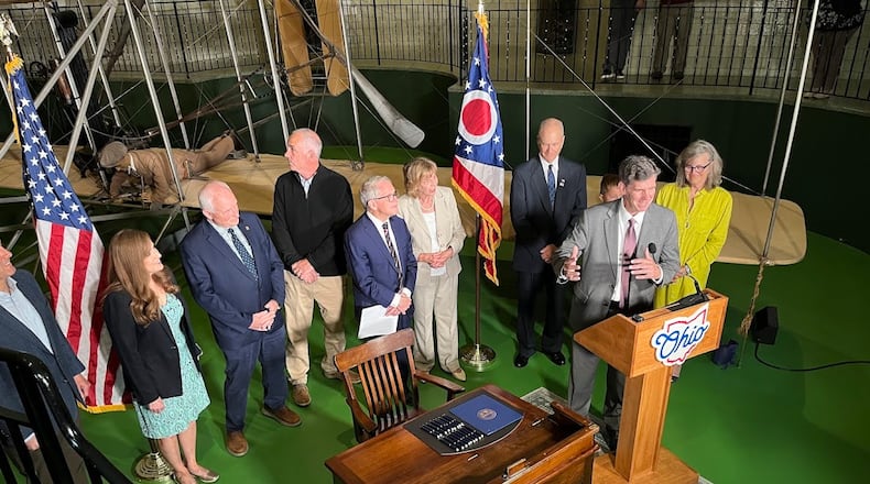 Brady Kress, president and chief executive of Dayton History, at the podium, explains the significance of the Wright Flyer III, the plane which is behind him and those assembled at Wright Hall Friday June 13, 2025 to celebrate legislation that made the Wright Flyer III Ohio's official airplane. THOMAS GNAU/STAFF