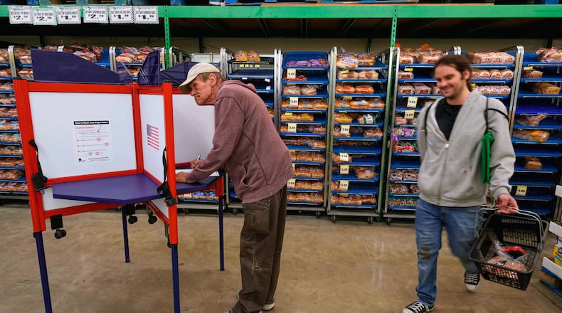 Bob Walser votes while a shopper walks past at the Checkers grocery store in Lawrence, Kan., Tuesday, Nov. 4, 2025. (AP Photo/Charlie Riedel)