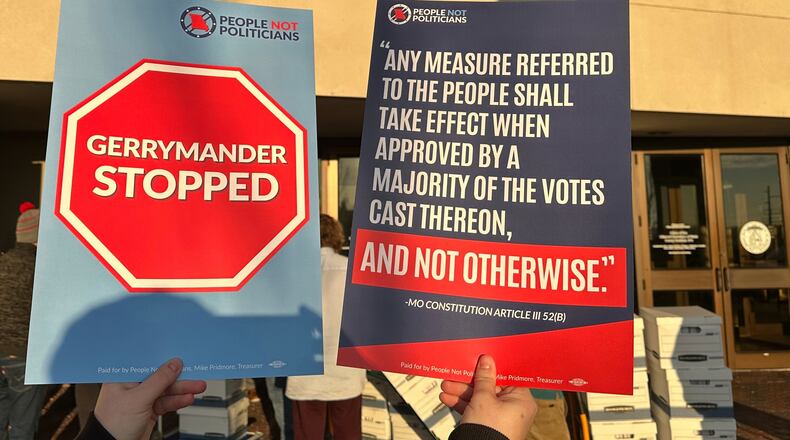 An opponent of new Missouri congressional districts approved by the Republican-led legislature holds signs outside the secretary of state's office in Jefferson City, Missouri, on Tuesday, Dec. 9, 2025, as petitions calling for a referendum election are delivered. (AP Photo/David A. Lieb)