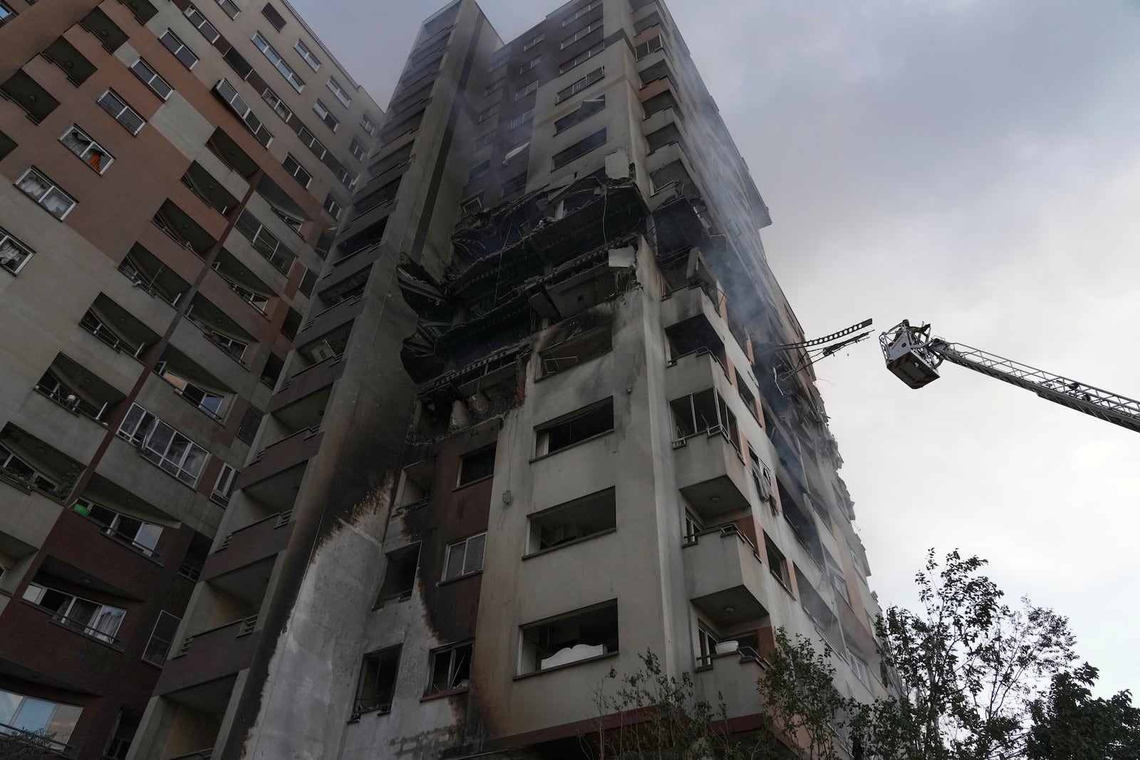 A firefighter stands on a crane at the scene of an explosion at a residence compound after Israeli attacks in Tehran, Friday, June 13, 2025. (AP Photo/Vahid Salemi)