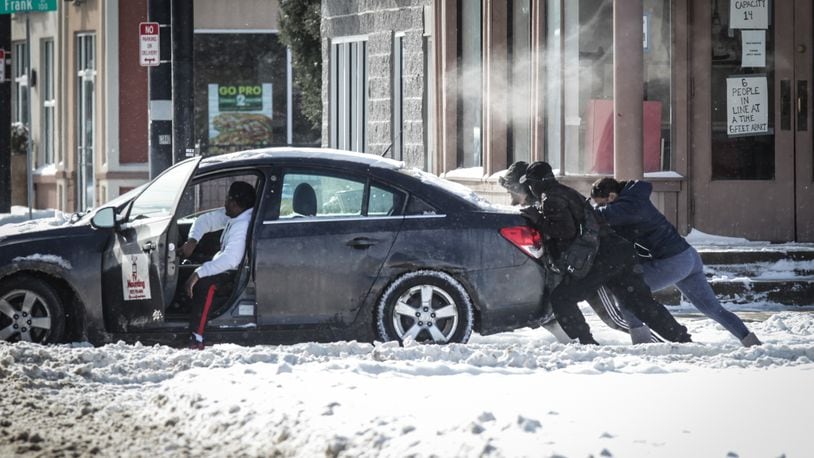 Good Samaritans help push a driver out of the ally on Brown St. Tuesday morning after a powerful winter storm dumped copious amounts of snow in the Miami Valley.