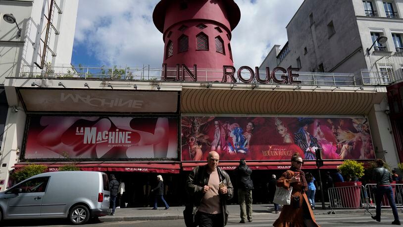 People walk past the Moulin Rouge (Red Mill) Thursday, April 25, 2024 in Paris. The windmill from the Moulin Rouge, the 19th century Parisian cabaret, has fallen off the roof overnight along with some of the letters in its name. (AP Photo/Thibault Camus)