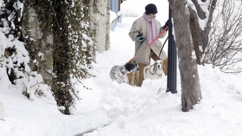 This 2008 photo shows a woman walking around the sidewalk with her three dogs because of almost a foot of snow covers the McPherson Town sidewalks in Dayton. STAFF/FILE
