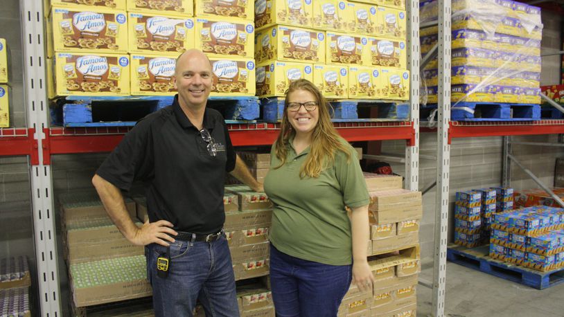 Mike Burke and Jamie Dailey stand next to shelves of food at Ahler’s Catering’s Vandalia warehouse that will be sorted and delivered to clients around the Miami Valley. KAITLIN SCHROEDER