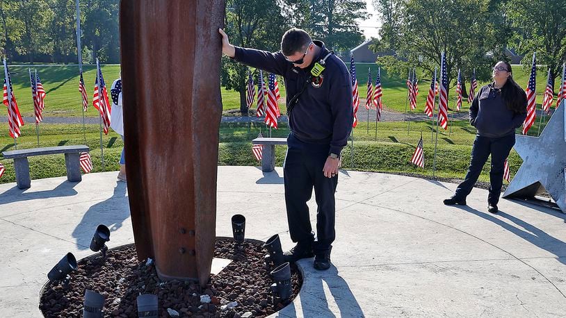 Mechanicsburg Firefighter Zach Sprinkle touches the World Trade Center artifact as he takes a moment while visiting Freedom Grove in Urbana for the 9/11 Memorial Service Monday, Sept. 11, 2023. BILL LACKEY/STAFF