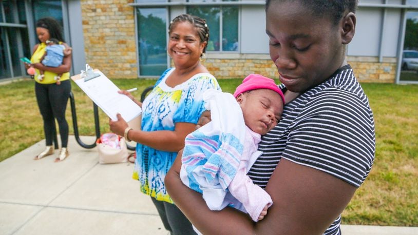 Tiara Thomas holds her baby So-Nae Turner as Natalie Jones, a certified community health worker from Butler County Moms and Babies First, looks on during a PRIM Community Action Team event outside Primary Health Solutions Health Center in Middletown, Tuesday, Aug. 29, 2017. Th PRIM team - consisting of local community leaders, Pastors, advocates and concerned citizens are working together to combat Infant Mortality. GREG LYNCH / STAFF