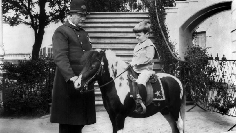 Quentin Roosevelt, son of President Theodore Roosevelt, rides his pony, accompanied by a police officer assigned to the White House, ca. 1902.
