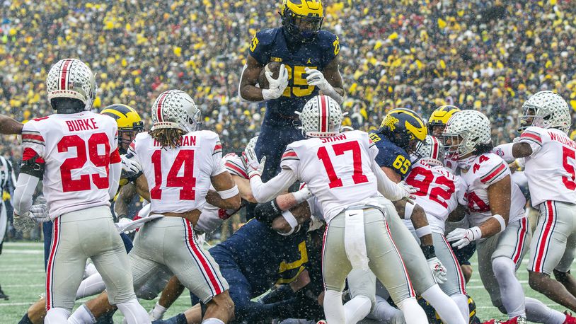 Michigan running back Hassan Haskins (25) leaps over Ohio State defenders for a touchdown in the second quarter of an NCAA college football game in Ann Arbor, Mich., Saturday, Nov. 27, 2021. (AP Photo/Tony Ding)