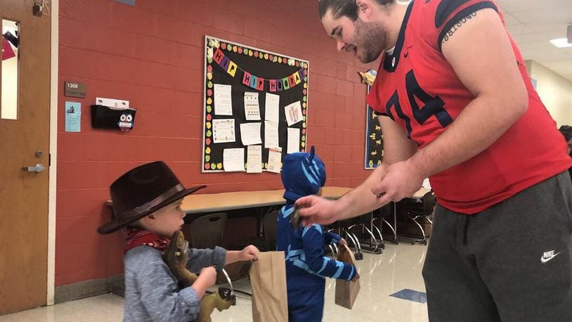 RYAN 8 – Former Dayton Flyers offensive lineman Ryan Culhane gives some candy to a young Trick-or-Treater during Halloween celebrations at Horace Mann Elementary in 2018 . CONTRIBUTED
