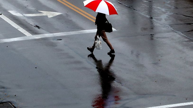 A man and his umbrella are reflected in wet pavement as he crosses Bechtle Avenue in the rain. BILL LACKEY/STAFF